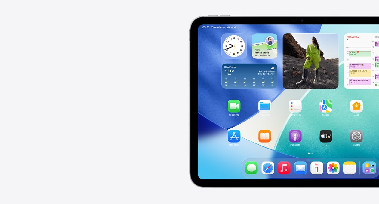 Um iPad na horizontal mostrando apenas o lado esquerdo da Tela de Início com widgets organizados, incluindo relógio translúcido com o efeito do Liquid Glass, app Buscar, widget Tempo, duas linhas de apps menores e o Dock