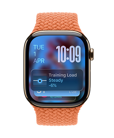 Apple Watch in Gold Titanium with a braided strap in Tangerine, face shows date at top left, time with stacked numerals at top right, Training Load widget at the bottom, all in translucent Liquid Glass