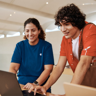 Una empleada de un Apple Store y un cliente, ambos de pie, interactúan con un MacBook.