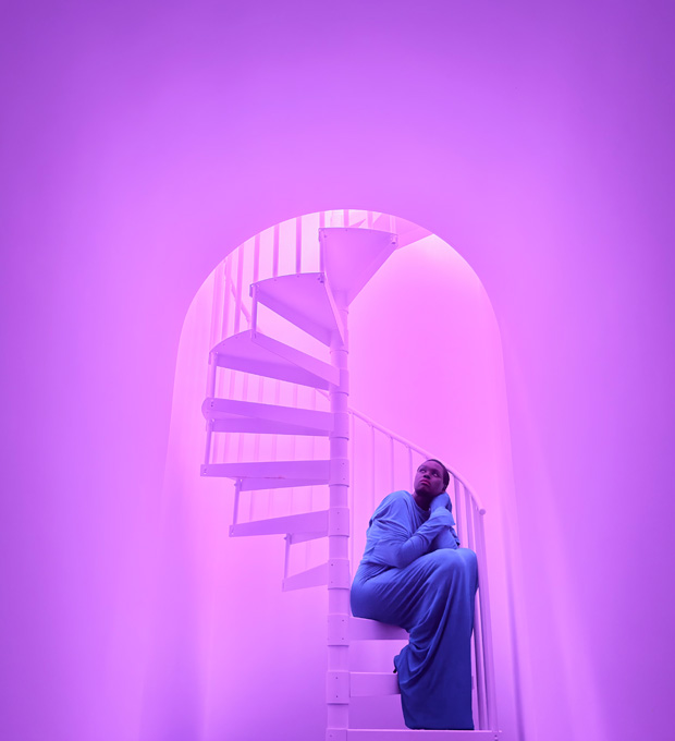 Nahaufnahme einer Frau, die auf einer Wendeltreppe sitzt, um die Fähigkeiten des Pro Kamera-Systems bei wenig Licht zu demonstrieren.